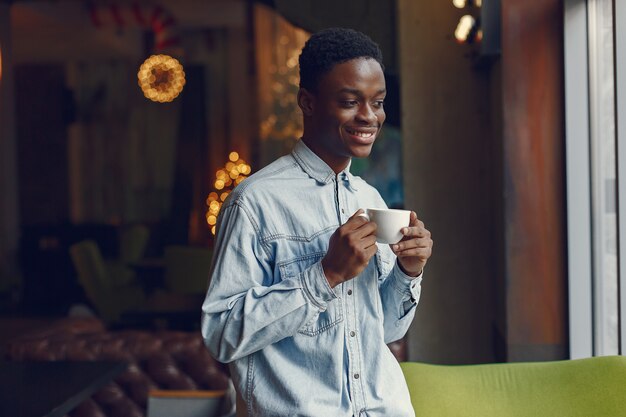 Black man standing in a cafe and drinking a coffee