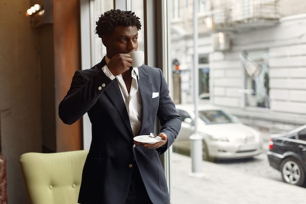 Black man standing in a cafe and drinking a coffee