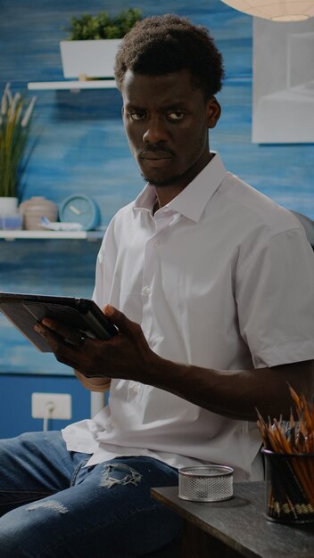 Черный человек с художественными навыками, используя планшет для дизайна вазы в мастерской студии. Человек афро-американской национальности, создающий рисунок на белом холсте и мольберте с помощью цифровых технологий