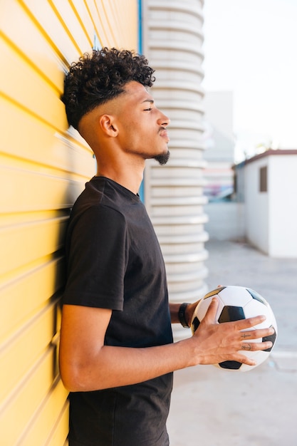 Black man with ball standing against wall