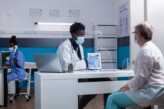 Foto gratuita uomo di colore con professione di medico che tiene raggi x su tablet moderno