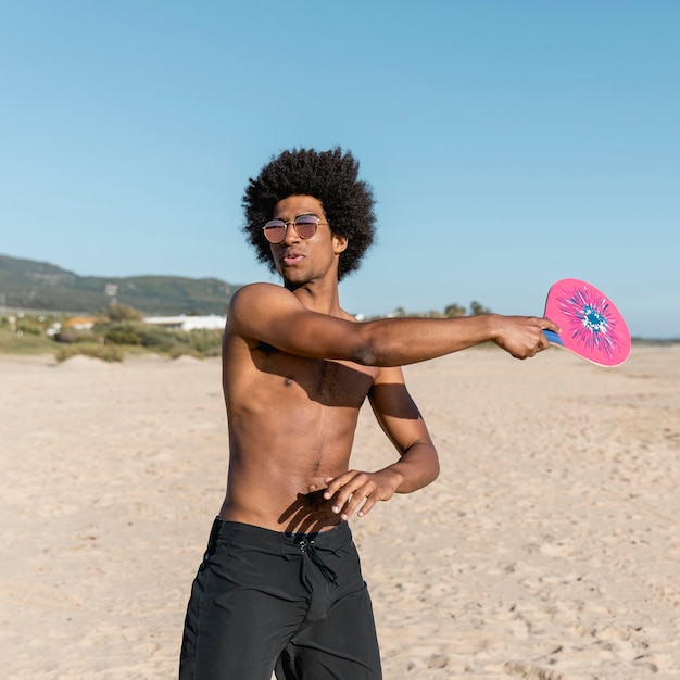 Black man with tennis racket on beach