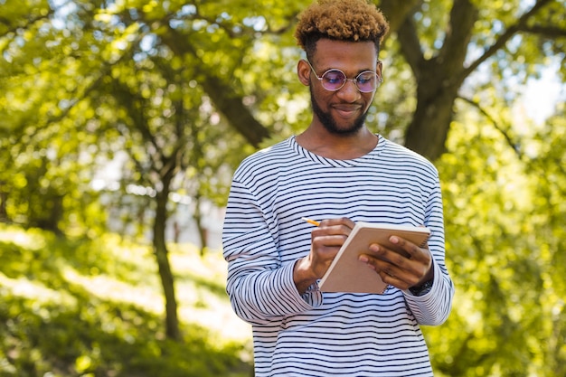 Black man writing in notepad in park