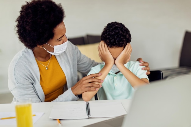 Black mother comforting her son who is feeling stressed out while learning at home during COVID-19 pandemic.