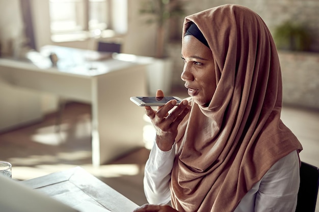 사무실에서 일하는 동안 휴대전화로 음성 메시지를 녹음하는 흑인 이슬람 기업가