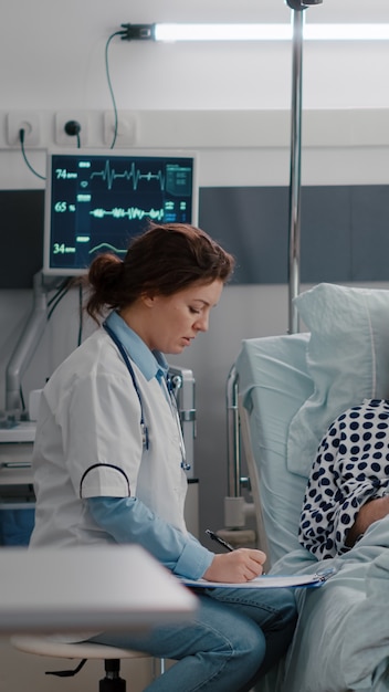 병원 병동에서 IV 체액 드립 백에 비타민을 주입하는 심장 박동을 모니터링하는 환자 바이탈을 검사하는 흑인 간호사