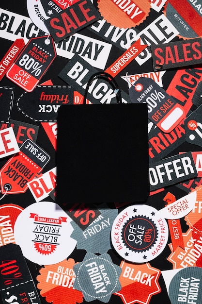 Free photo black paper bag lying on many colorful labels with sale offer