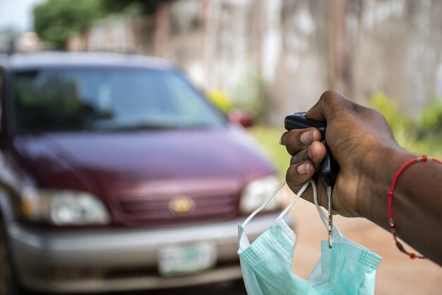 Black person using a car remote to unlock a car, holding a face mask