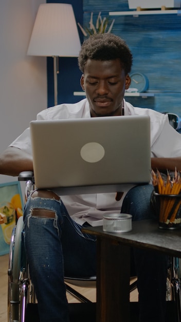 창의성 공간에서 예술적 영감을 얻기 위해 노트북 컴퓨터를 사용하는 휠체어를 탄 흑인. 현대 스튜디오에서 전문 걸작을 디자인하는 장애인 아프리카계 미국인 예술가