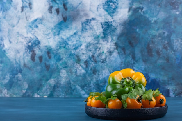 Black plate of bell pepper and cherry tomatoes on blue background.
