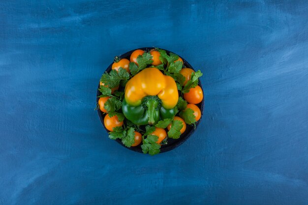 Black plate of bell pepper and cherry tomatoes on blue table.