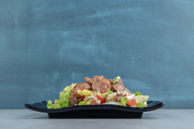 A black plate of chicken fried meat and vegetable salad . 