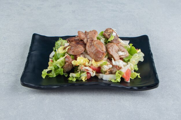 A black plate of chicken fried meat and vegetable salad . 