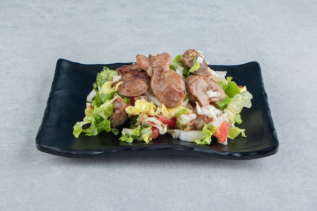 A black plate of chicken fried meat and vegetable salad . 