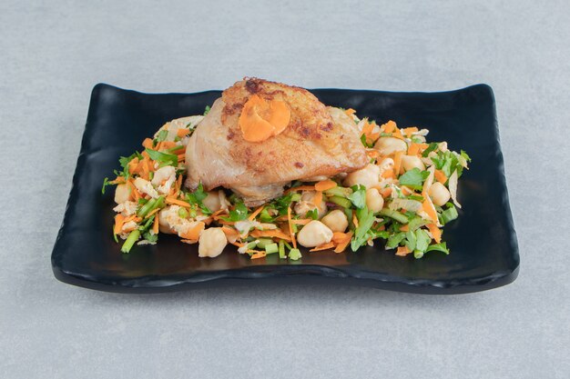 A black plate of chicken fried meat and vegetable salad . 