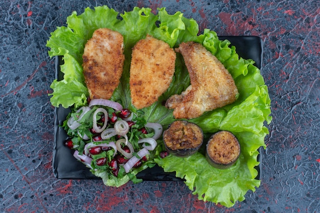 A black plate of chicken meat with vegetables .