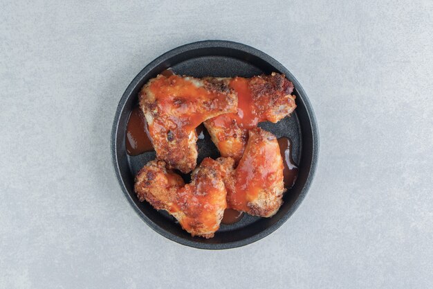 A black plate of fried meat in tomato sauce . 