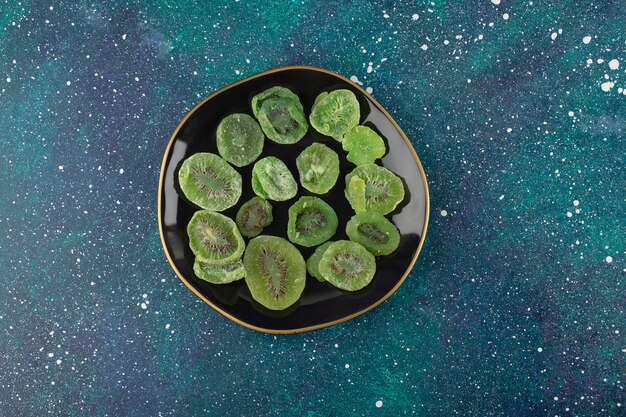 A black plate full of dried kiwi fruit .