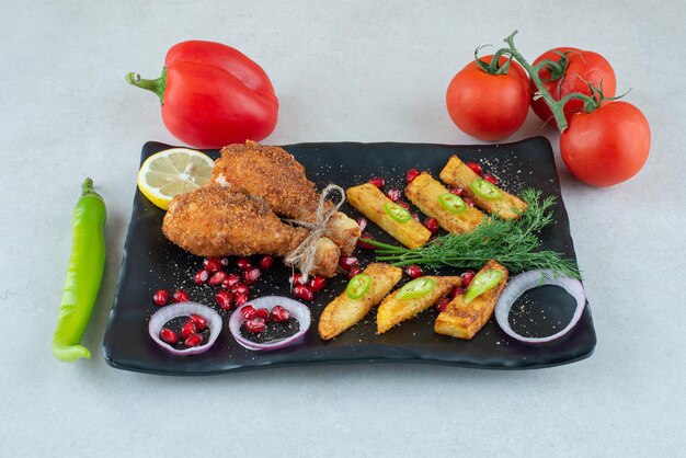 A black plate full of fried chicken with tomatoes and pepper.