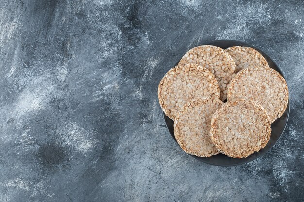 A black plate full of puffed rice bread on a marble surface .