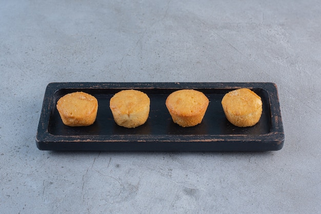 Black plate of mini sweet cakes on stone.