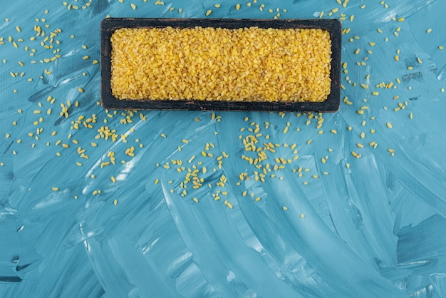 Бесплатное фото Черная тарелка сырого сухого риса на синем фоне.