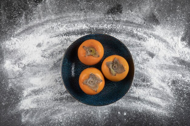 Черная тарелка спелых фруктов хурмы на черной поверхности