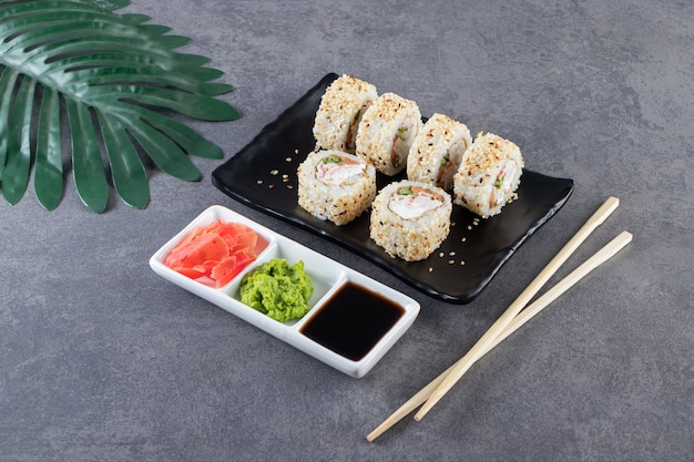 Piatto nero di sushi rotoli con semi di sesamo su sfondo di pietra.