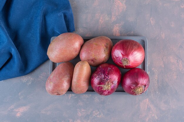 Black plate of sweet potatoes and red onions on stone surface