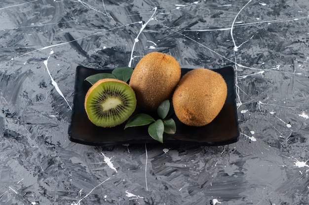 Free photo black plate of whole kiwi fruits placed on marble table.