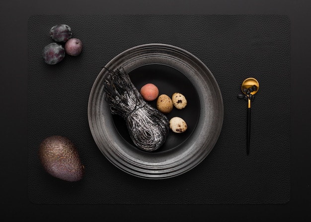 Black plate with black pasta and quail eggs on a dark background