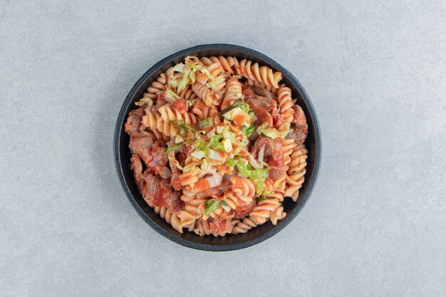 A black plate with spiral pasta with herbs . 