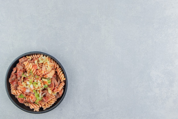 A black plate with spiral pasta with herbs . 