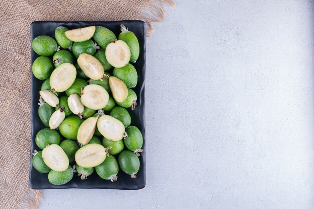 Black platter of feijoas on marble background.