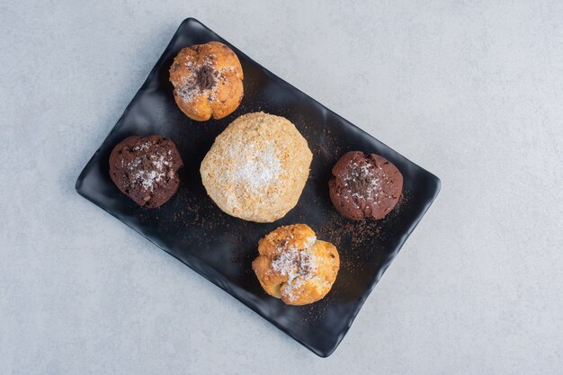 Black platter with various cupcakes on marble surface