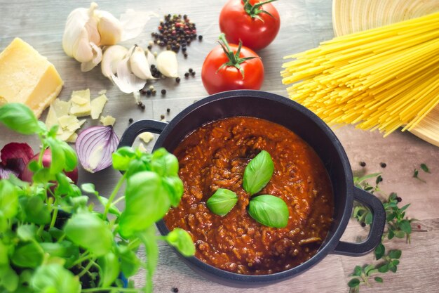 Black pot cooking sauce bolognese with ingredients on a wooden table