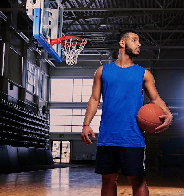 Free photo black professional basketball player holds a ball over the hoop in a game hall.