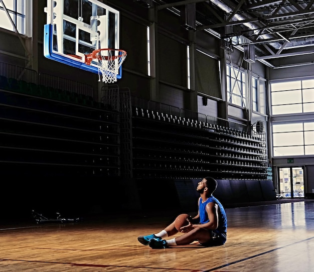 흑인 프로 농구 선수가 게임 홀의 후프 아래 필드에 앉아 있습니다.