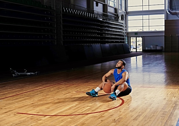 Black professional basketball player sits on a floor in a game hall.