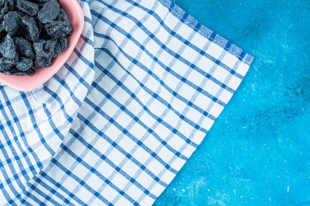 Black raisins in a bowl on tea towel , on the blue table. 