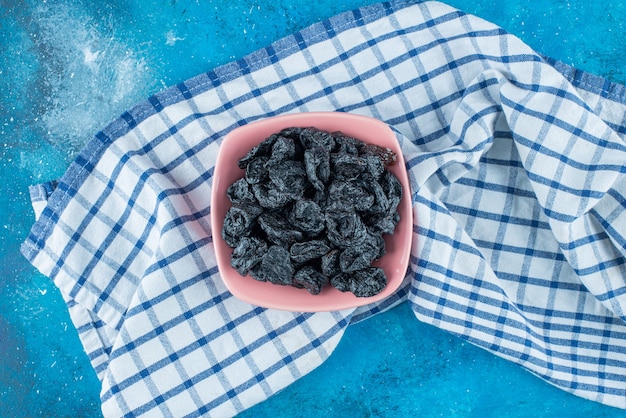 Black raisins in a bowl on tea towel , on the blue table. 