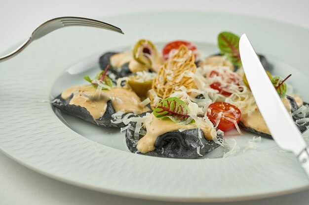 Черные равиоли с мясом, нарезанным на вилке, соусом и помидорами в тарелке Premium Фотографии