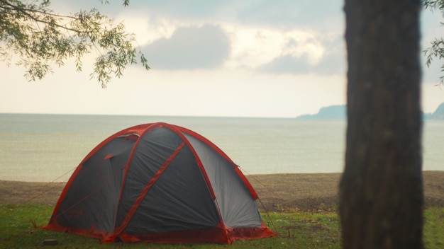 Черно-красная палатка на берегу возле красивого моря под облачным небом