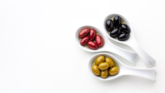 Black red yellow olives in spoons with copy space