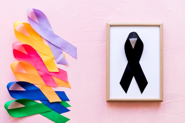 Free photo black ribbon on white wooden frame near the row of colorful awareness ribbon