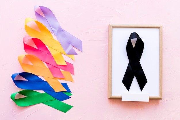 Black ribbon on white wooden frame near the row of colorful awareness ribbon