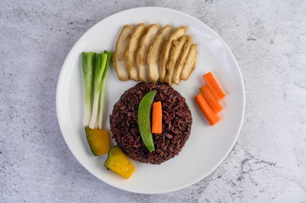 Black rice on a plate with pumpkin, peas, carrots, baby corn and steamed chicken breast.