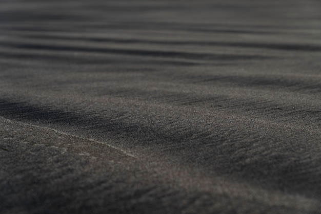 Макросъемка пляжа с черным песком. Шелковистая черная текстура пляжа с малой глубиной резкости. Минималистичный черный фон. Тенерифе Вулканический песчаный берег.