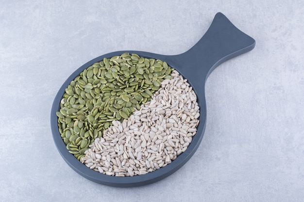 Black serving pan full of peeled sunflower seeds and pepitas on marble surface