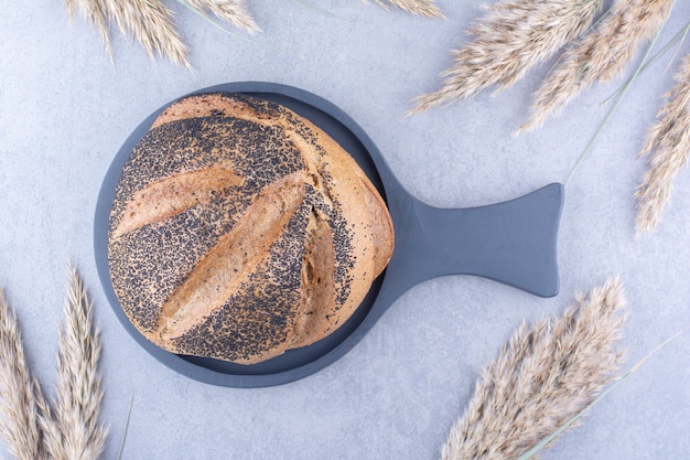 Pagnotta di pane ricoperta di sesamo nero su una padella, accanto a gambi di erba secca sulla superficie di marmo